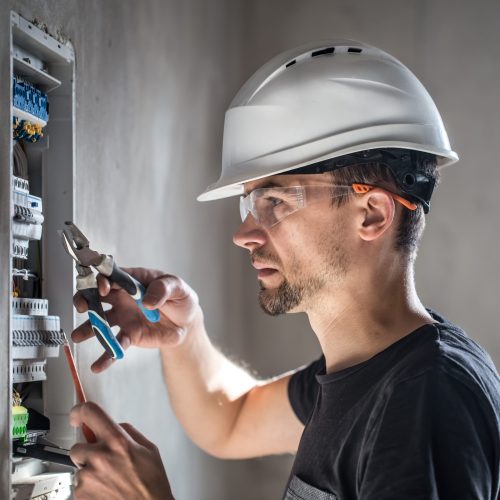 Man, an electrical technician working in a switchboard with fuses. Installation and connection of electrical equipment. Professional with tools in hand. concept of complex work, space for text.